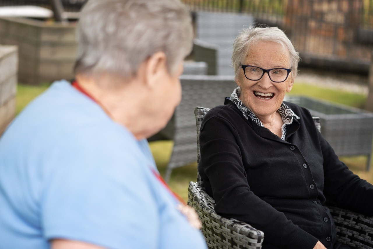 2 people are sat outside smiling whilst chatting