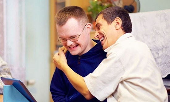 Two young people laughing. One has their arms around the other in a hug.