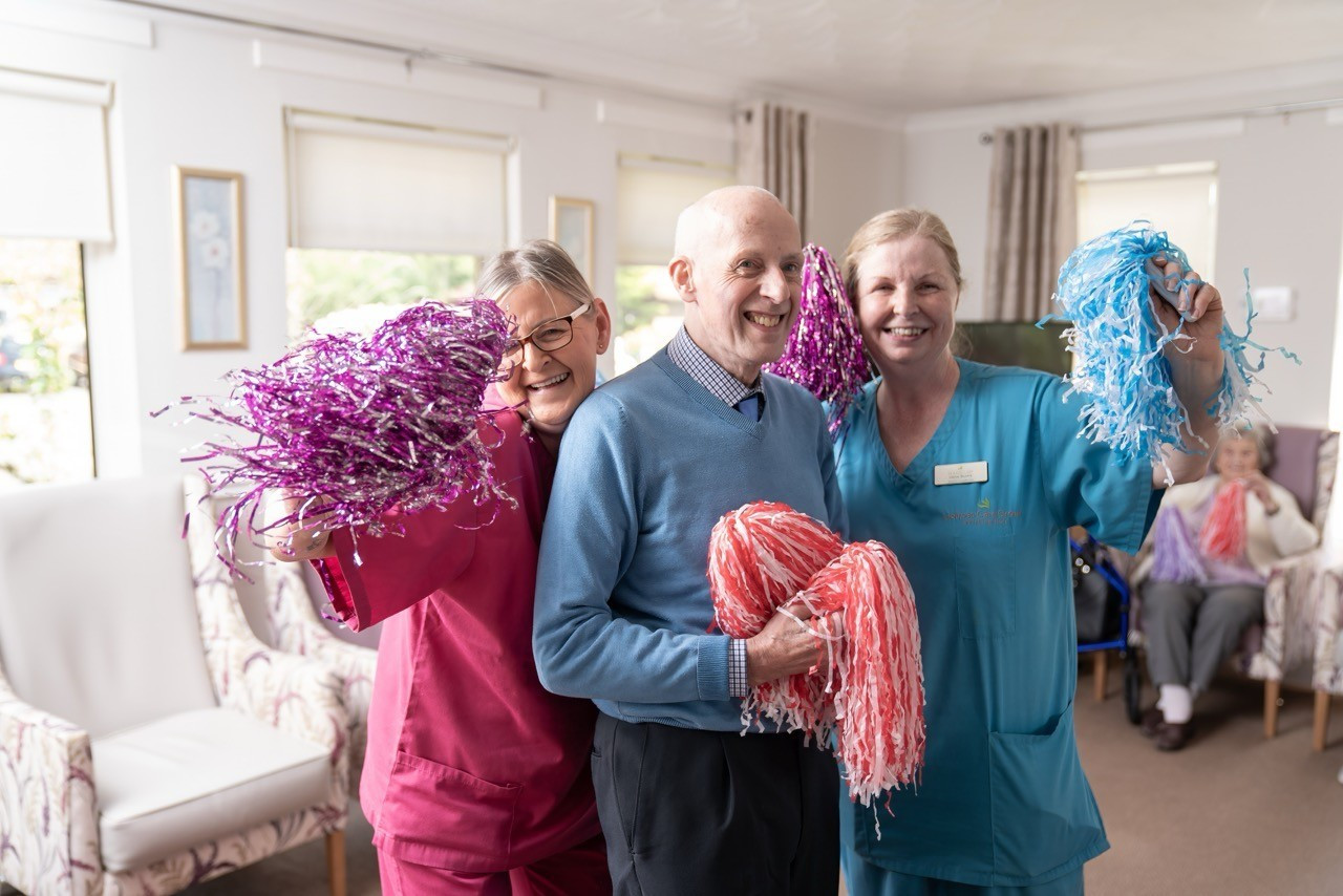 3 individuals are stood smiling to camera and shaking pom poms